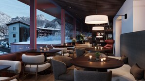 Un restaurante moderno con amplios ventanales que ofrecen vistas a la montaña, mesas y sillas de madera e iluminación ambiental.