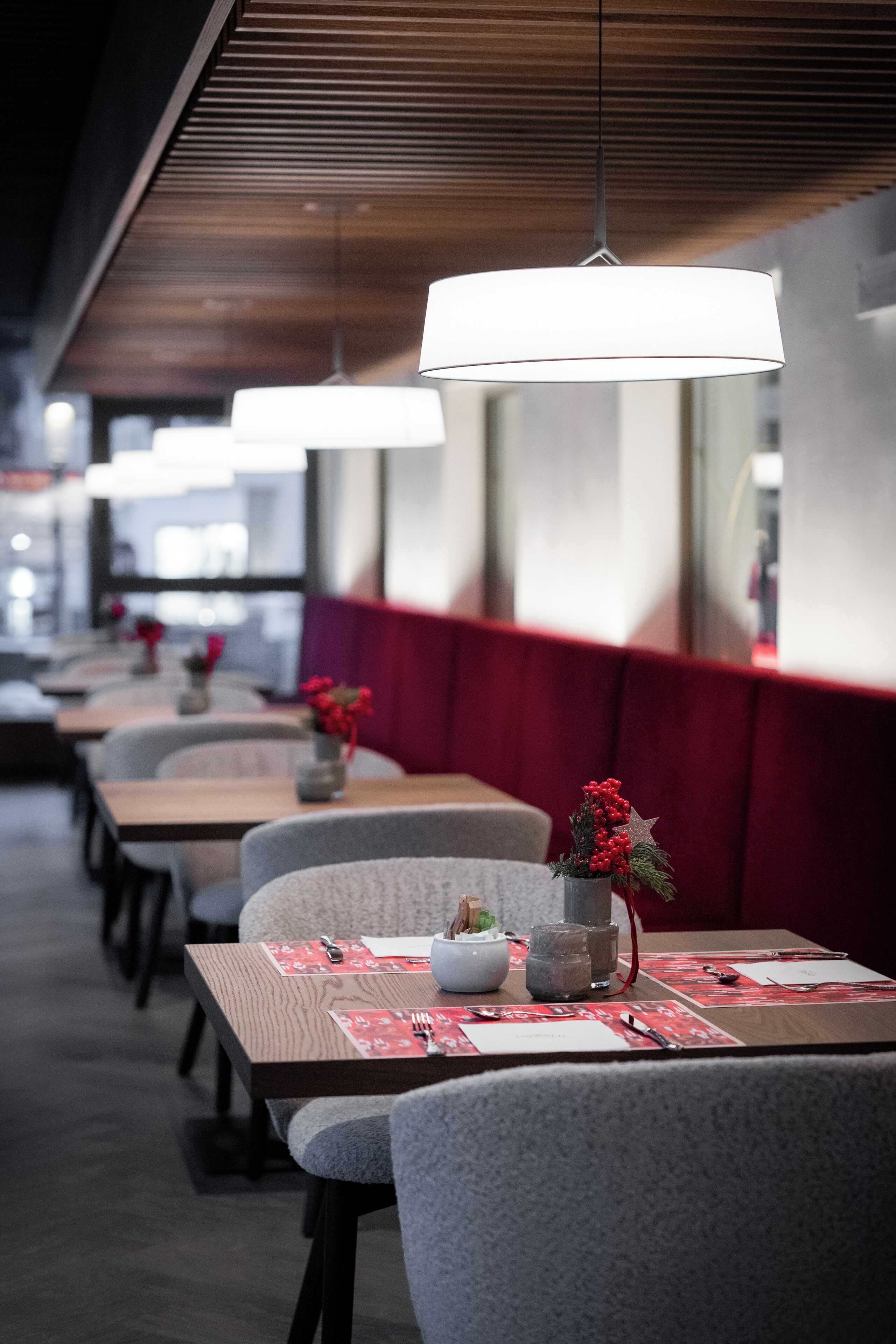 A row of tables with grey chairs, each with a red placemat and a small vase with red flowers.