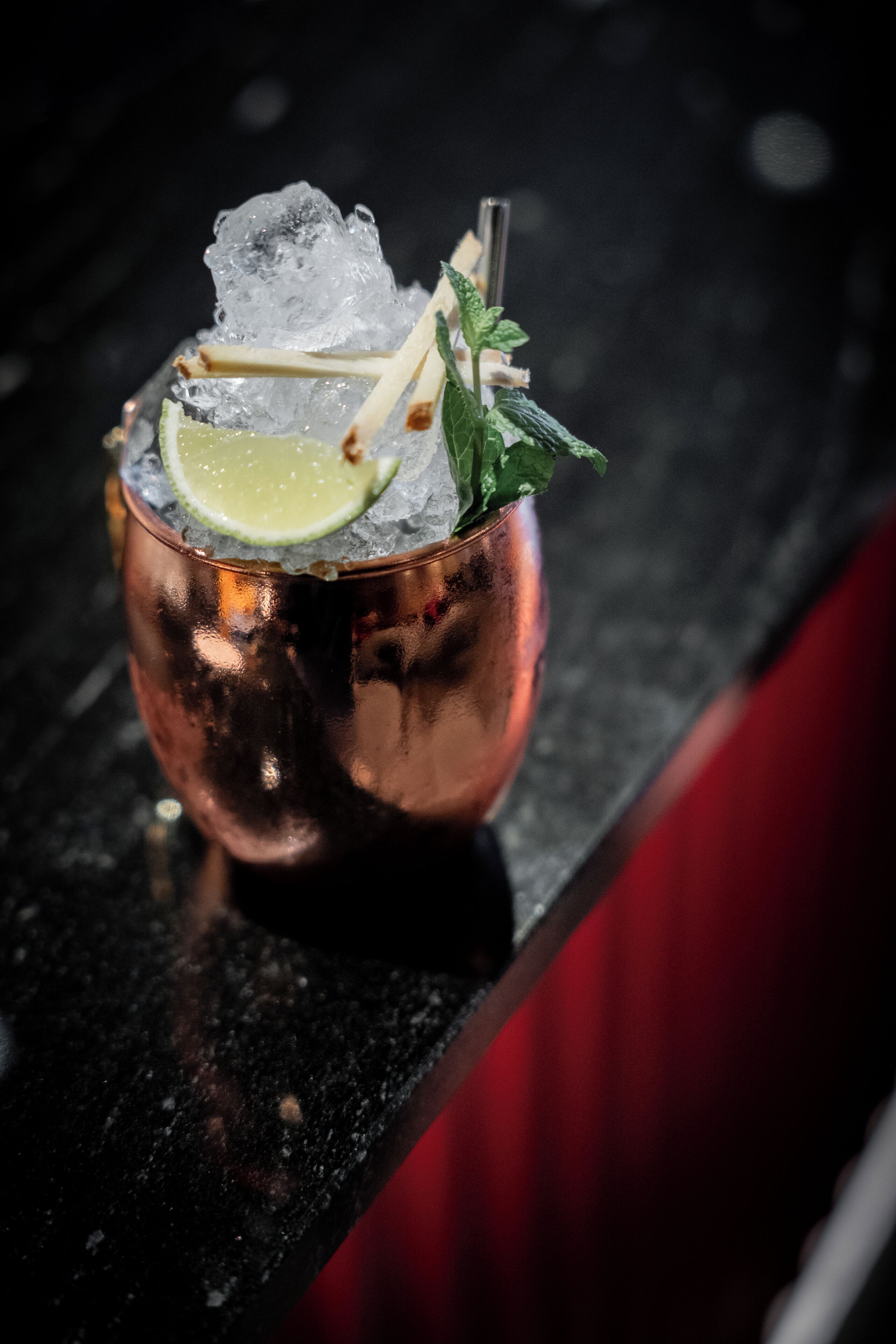 Een koperen cocktailglas met ijs, limoen, munt en een rietje op een bargedeelte.