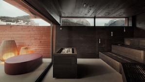 Un interior moderno con techo de madera, un ventanal con vistas a la montaña, una zona de estar roja y una estructura rectangular negra.