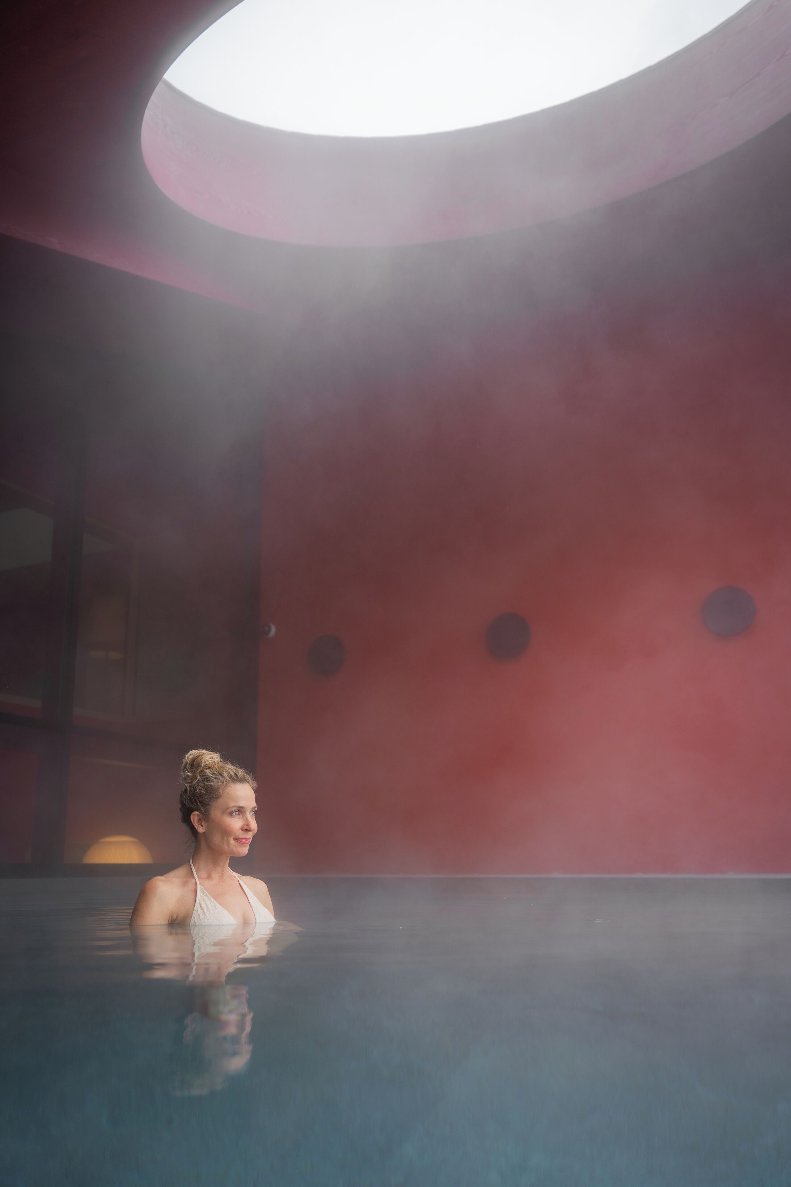 A person in a large indoor pool with a circular skylight above.