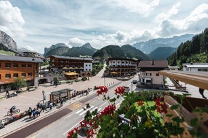 Una plaza de pueblo con edificios, un paso de peatones y montañas al fondo.