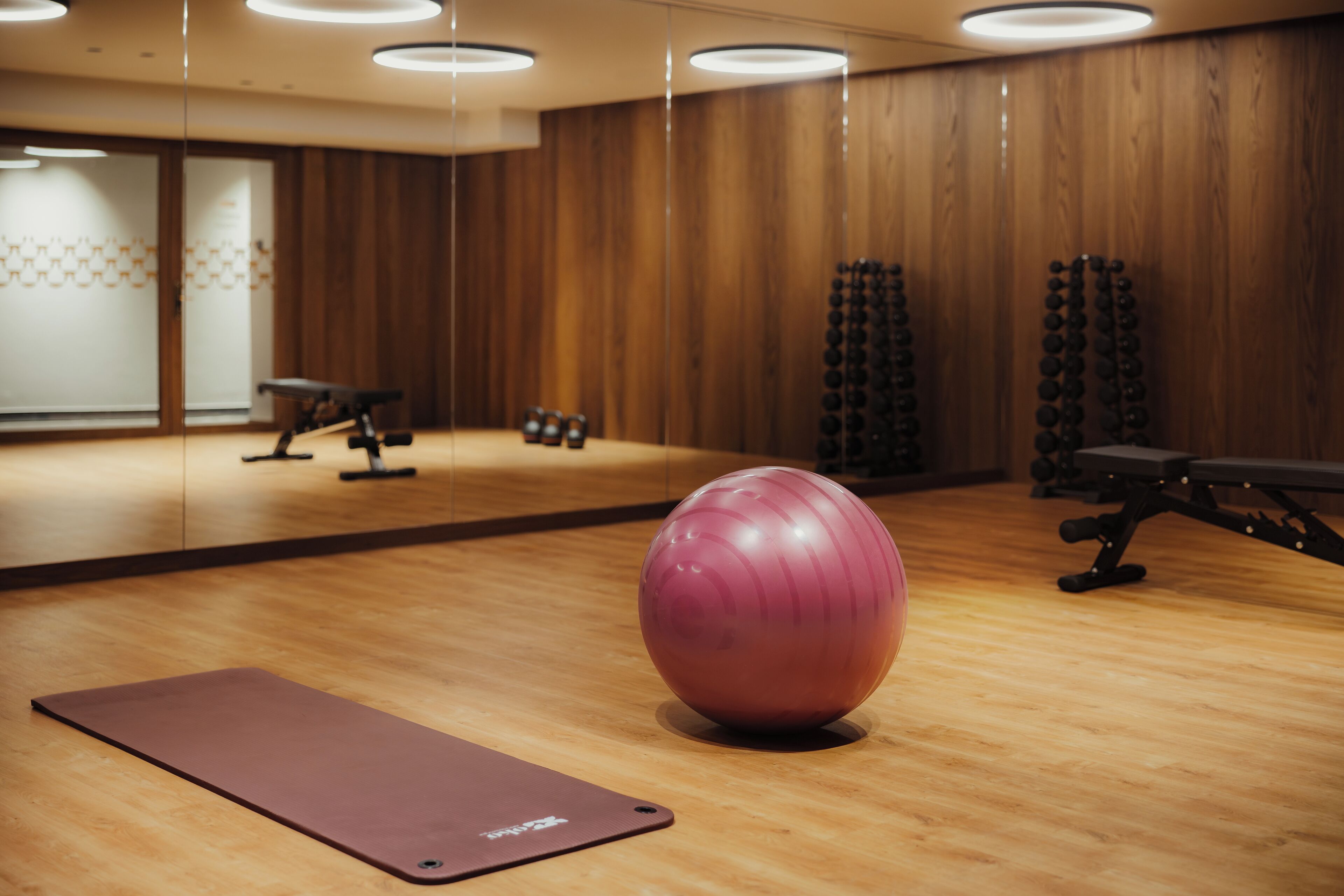 Academia com piso de madeira, equipamentos de ginástica e uma bola de exercícios rosa.