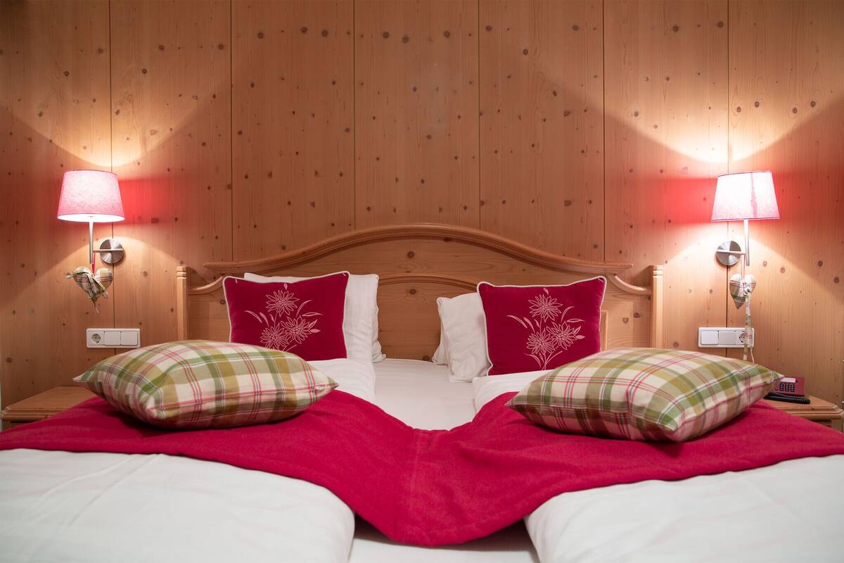 A hotel room with a wooden headboard, two bedside lamps, a bed with red and white bedding, and two plaid pillows.