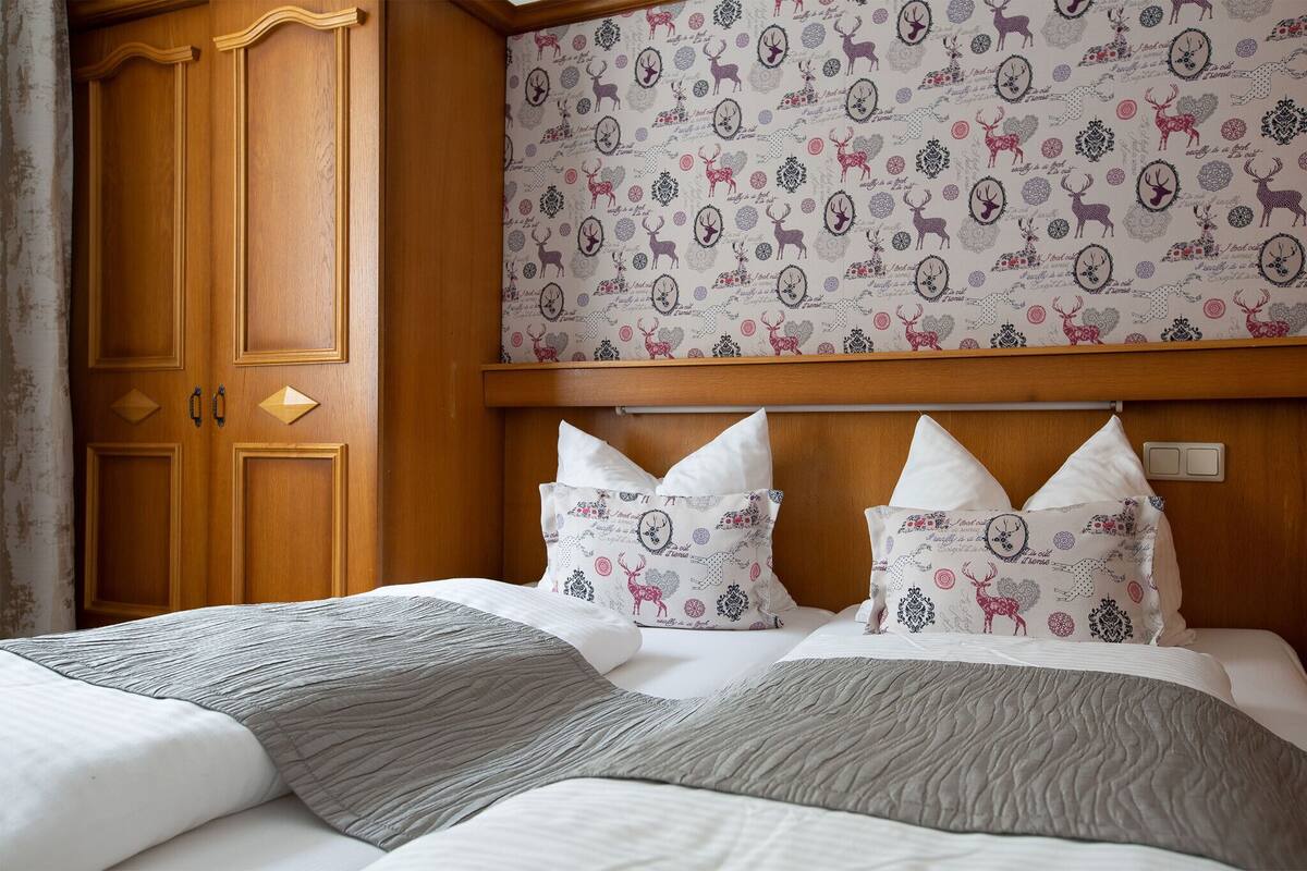A hotel room with a large wooden wardrobe, a patterned headboard, and a neatly made bed with pillows.