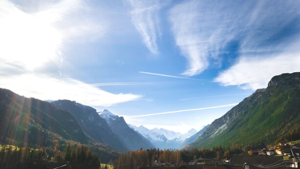 Une vue panoramique d’un paysage montagneux, avec une vallée, des maisons et un ciel dégagé.