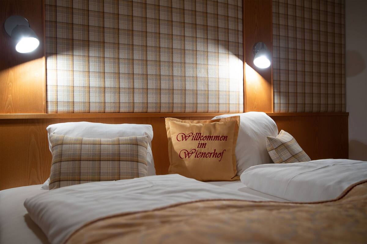 A hotel room with a bed, two pillows, a welcome pillow, and two wall-mounted lights.