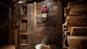 A rustic wooden interior with a wooden door, a heart-shaped decoration, and a basket of firewood. - Genuss-Boutique B&B Wienerhof (Trins)