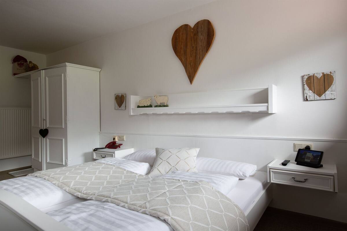 A neatly arranged bedroom with a large bed, a bedside table with a tablet, and a wardrobe.