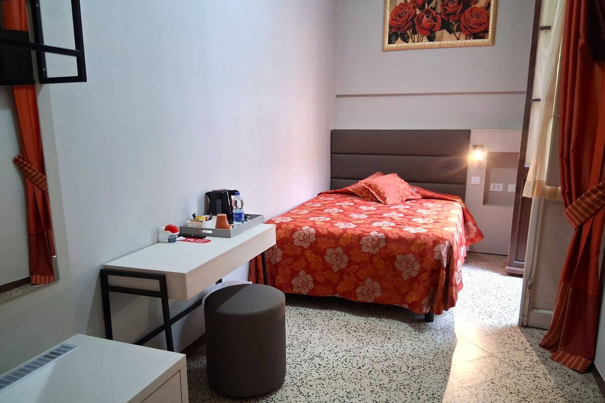 Une chambre d’hôtel avec un lit, un bureau, une chaise, une poubelle et un tableau au mur.