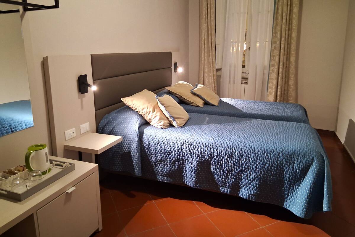 Une chambre avec deux lits, une table de chevet, un petit bureau avec une bouilloire et un miroir.