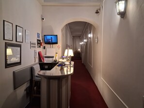 Ein Hotelgang mit einer Rezeption, einem Flachbildfernseher, gerahmten Zertifikaten und einem Rauchverbot-Schild.