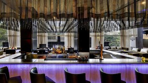 Un área de bar moderna con una barra alargada, taburetes y vistas al exterior a través de amplios ventanales.