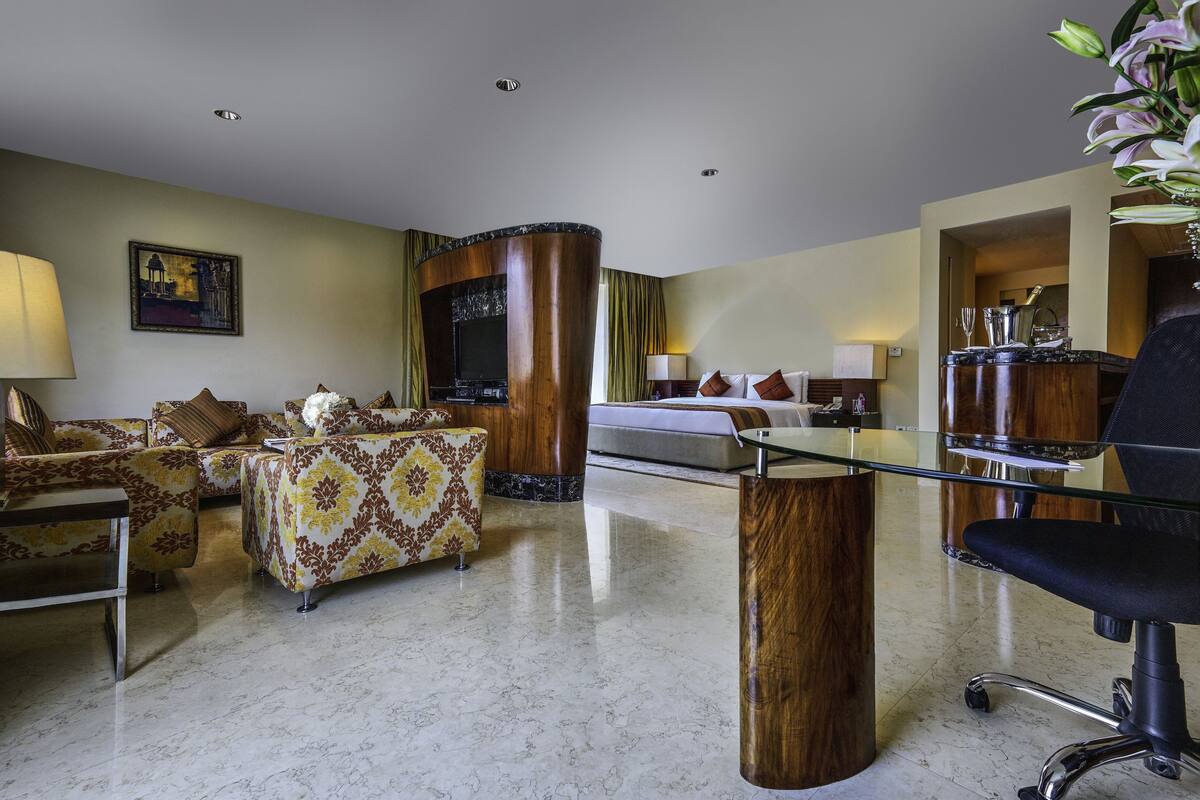 Ein modernes Hotelzimmer mit einer Sofagarnitur, einem Glastisch, einem Schreibtisch mit Stuhl und einem Fernseher.