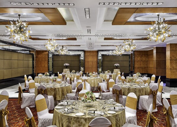 A banquet hall with round tables, gold sashes, and chandeliers.