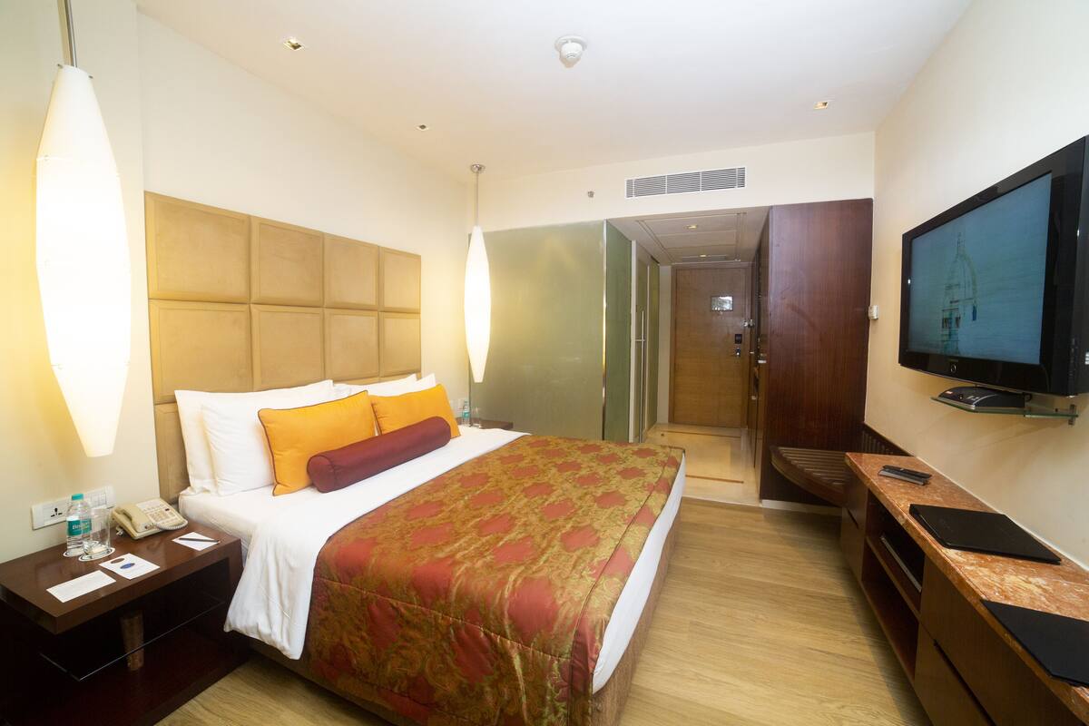 Ein Hotelzimmer mit Bett, Nachttisch, Fernseher und Schreibtisch mit Stuhl.