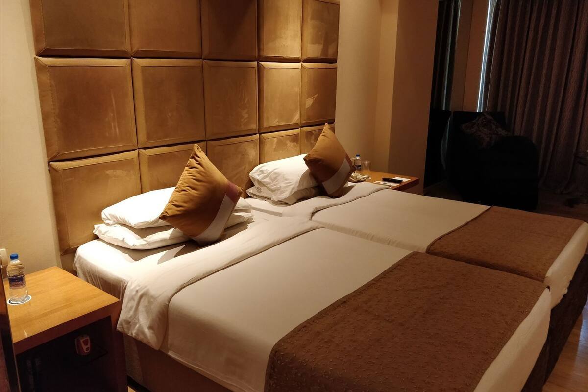 Ein Hotelzimmer mit einem großen Bett, einem hölzernen Kopfteil, einem Nachttisch mit einer Flasche und einem Sessel in der Ecke.