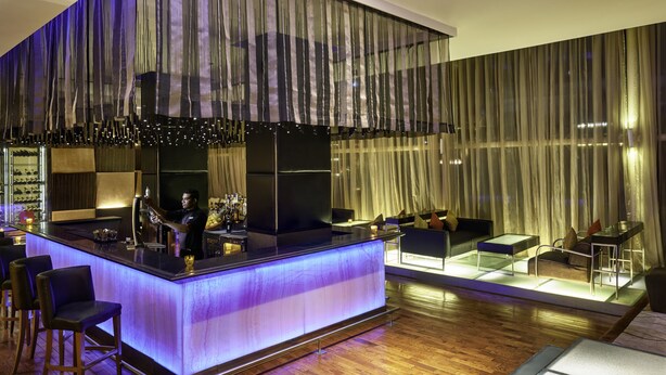 Zona de bar moderna con mostrador, taburetes y un área de estar con sofás y una mesa de centro.
