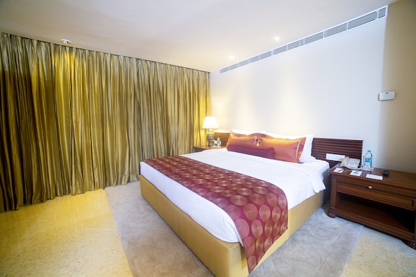 Una habitación de hotel con una cama grande, una mesita de noche, una lámpara y una cortina.