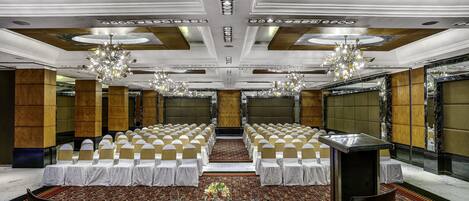 Un salón de banquetes con filas de mesas y sillas, candelabros y suelo alfombrado.