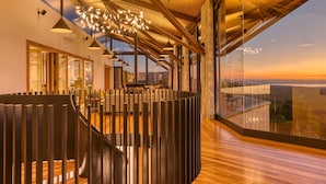 Un interior moderno con una escalera de madera, ventanas amplias y vistas al atardecer.