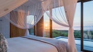 Un dormitorio con una cama grande, cortinas translúcidas y vistas al exterior.