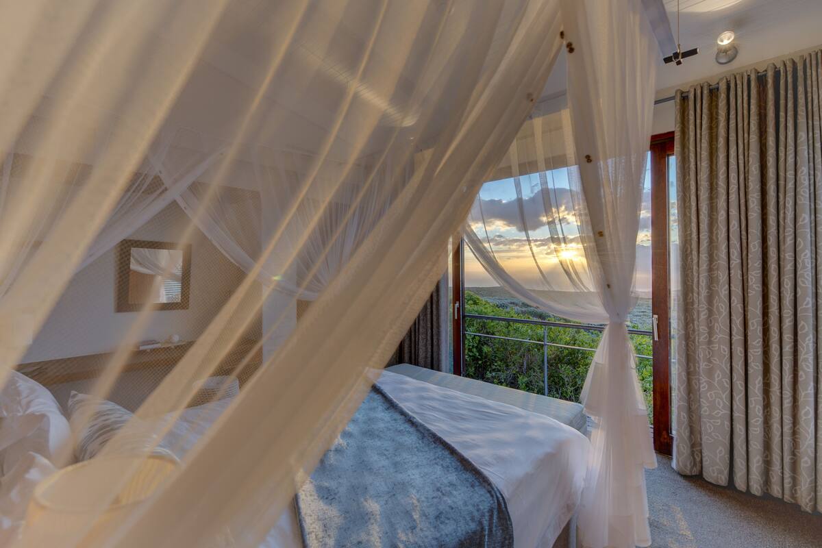 A bedroom with a bed, a window with curtains, and a view of the outdoors.