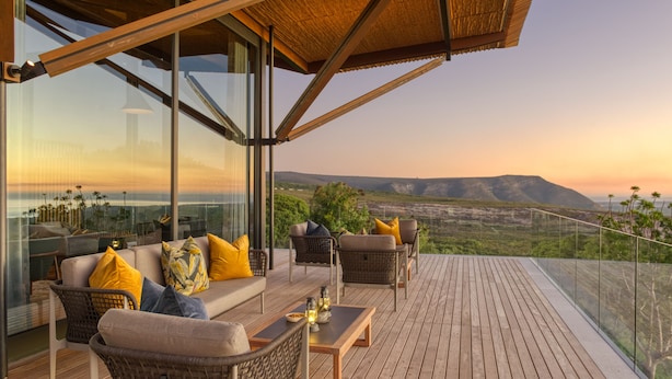 Un área de estar al aire libre con muebles de mimbre y cojines, con vistas a un paisaje pintoresco.