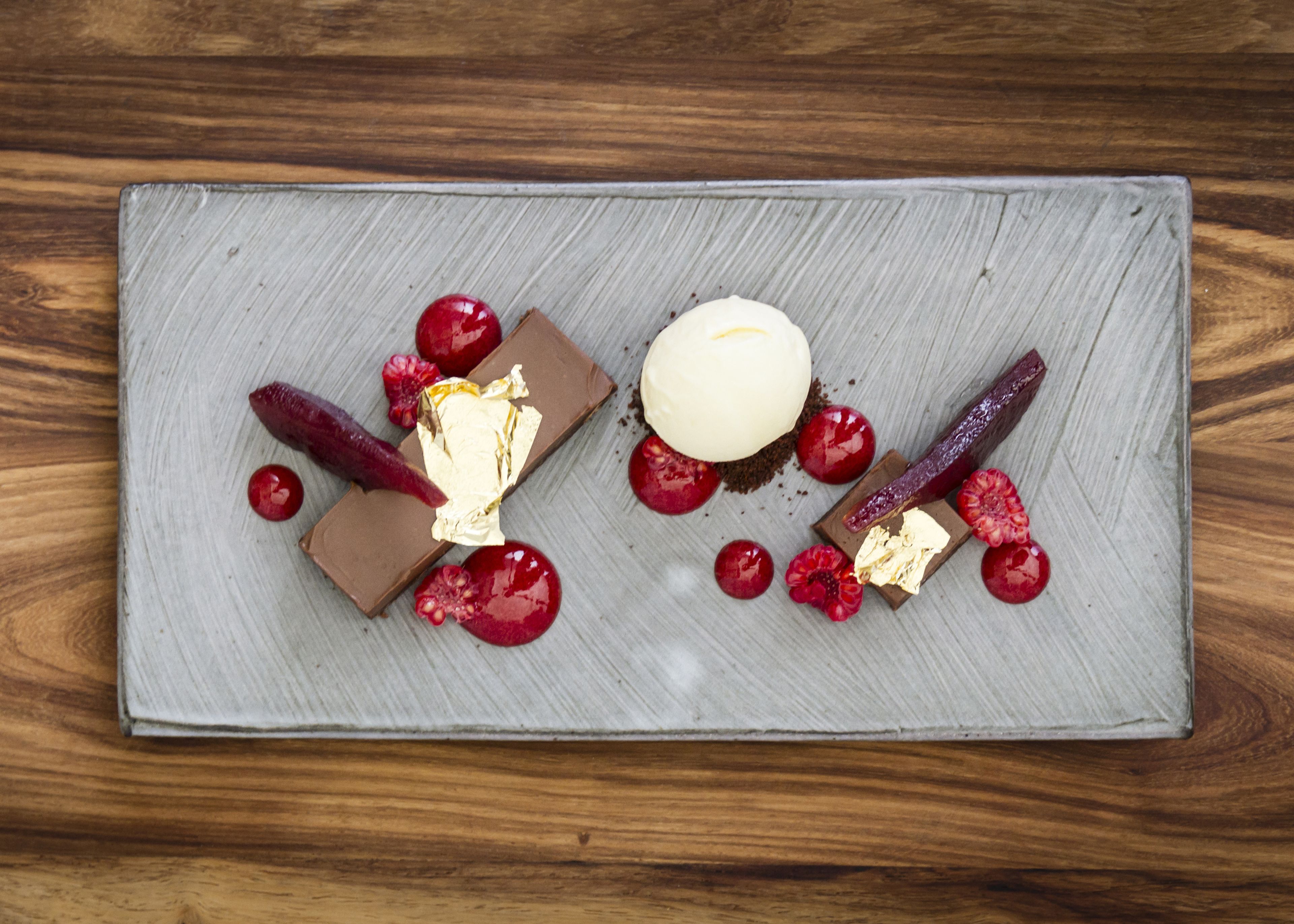 A dessert plate with chocolate, ice cream, and berries on a wooden table.