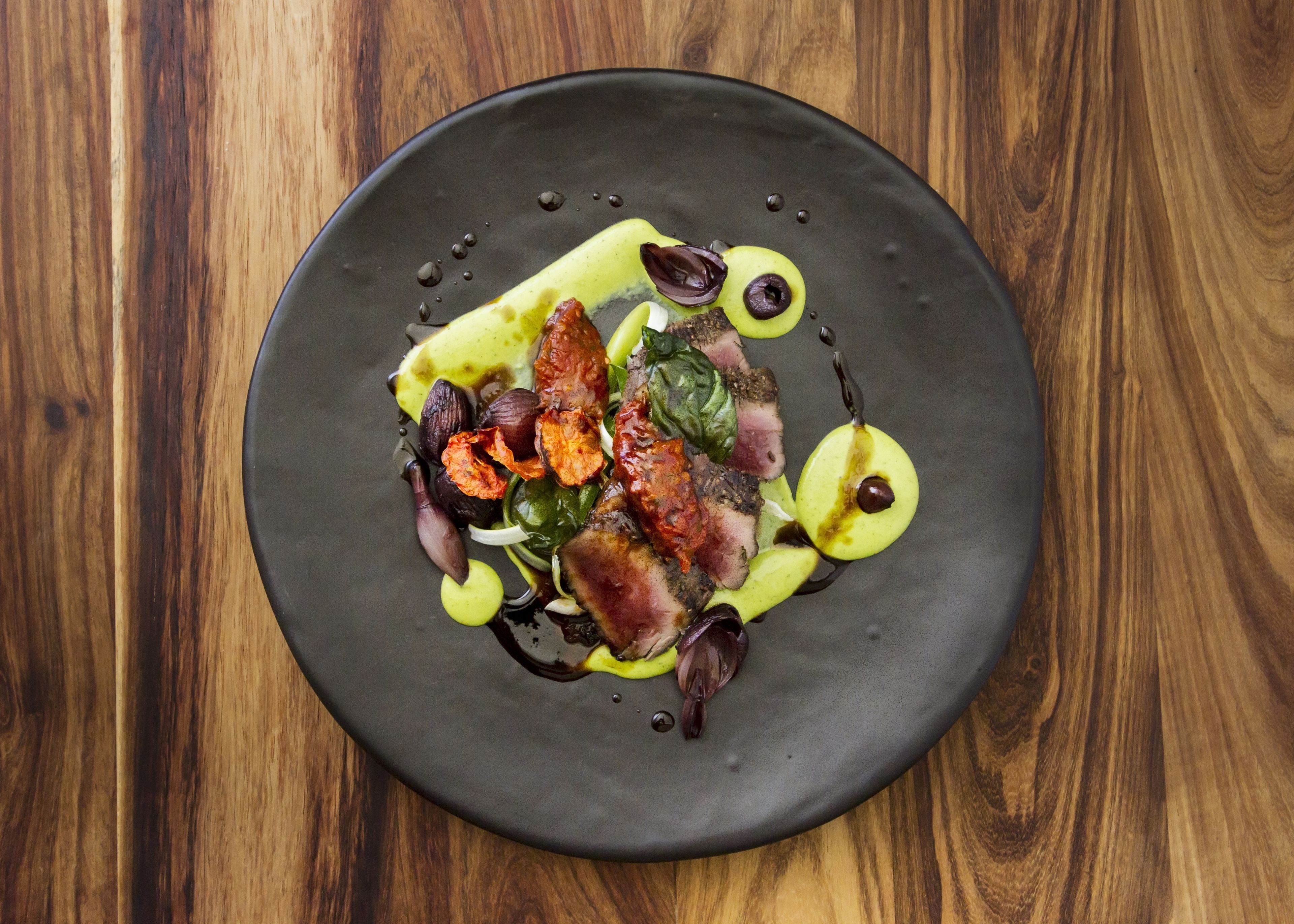 A round black plate with a variety of food items including meat, vegetables, and possibly some sauce, on a wooden table.