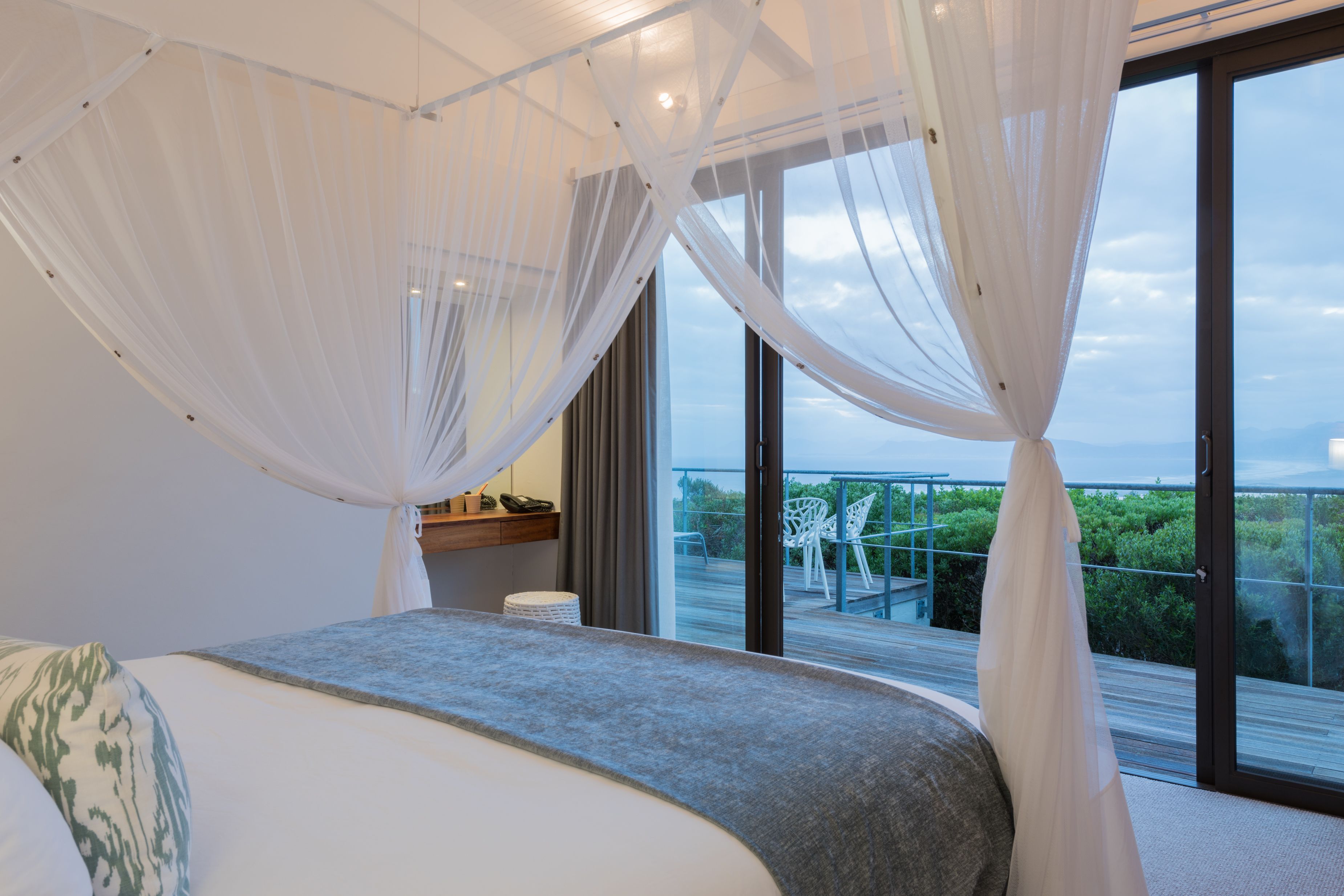 Quarto com cama grande, cortinas leves e varanda com vista para o verde.