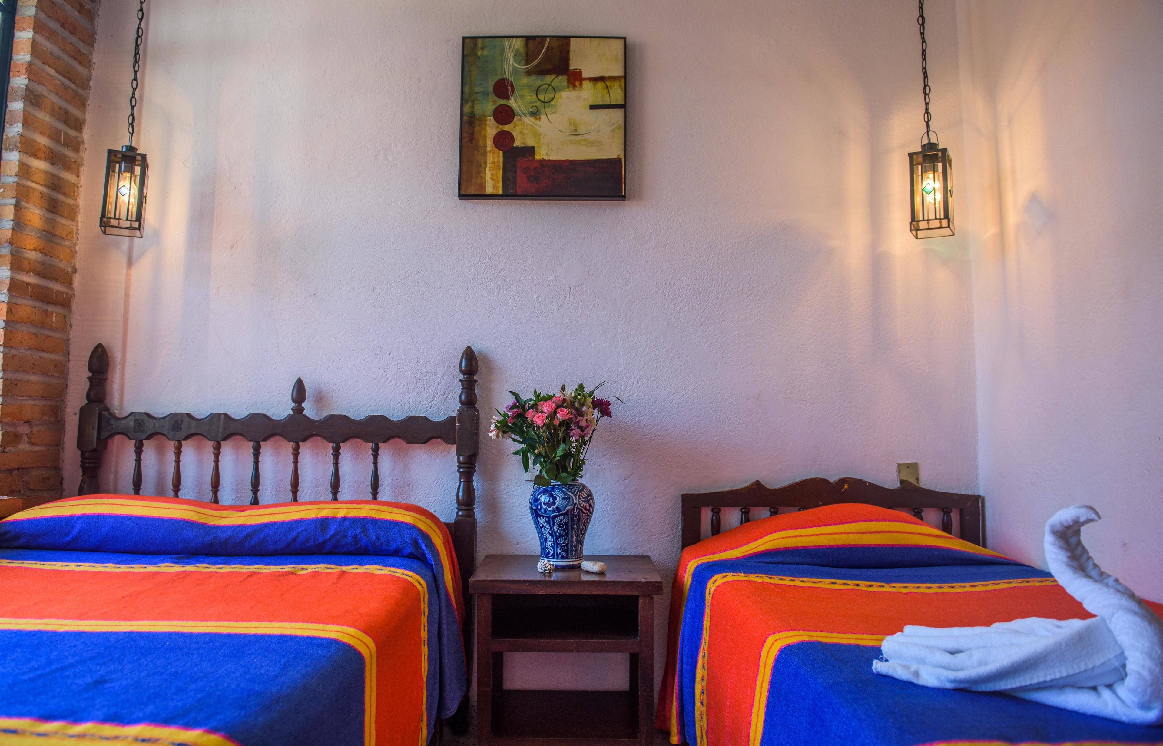 Habitación de hotel con dos camas, una mesita de noche con un jarrón de flores y un cuadro en la pared.