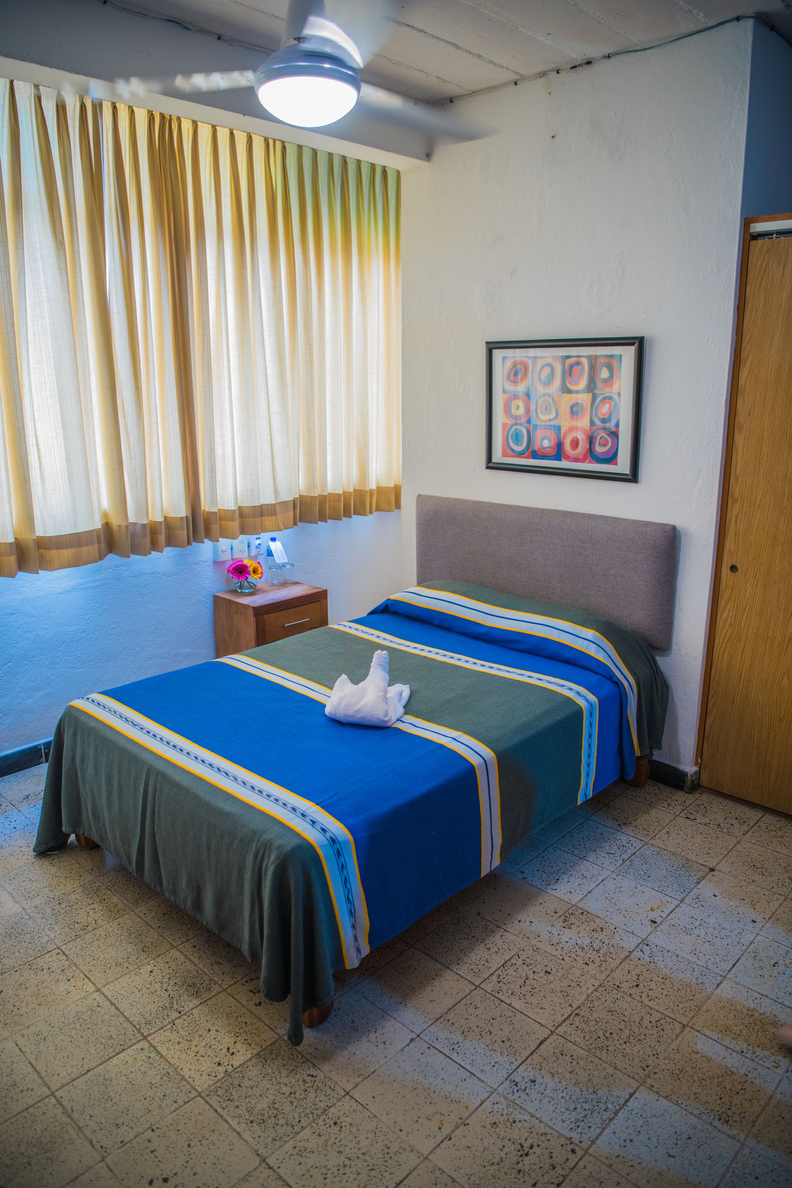 A hotel room with a bed, a nightstand, a framed picture, and a window with curtains.