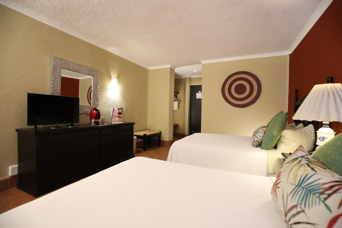 A hotel room with two beds, a TV on a dresser, a mirror, a target decoration on the wall, and a lamp.