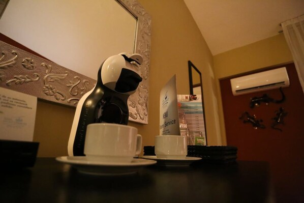 A coffee machine with a cup and saucer on a table, a menu stand, and an air conditioning unit on the wall. - Hotel Montetaxco (Taxco)
