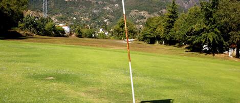 A golf flag on a flagpole in a grassy field with a mountain in the background.