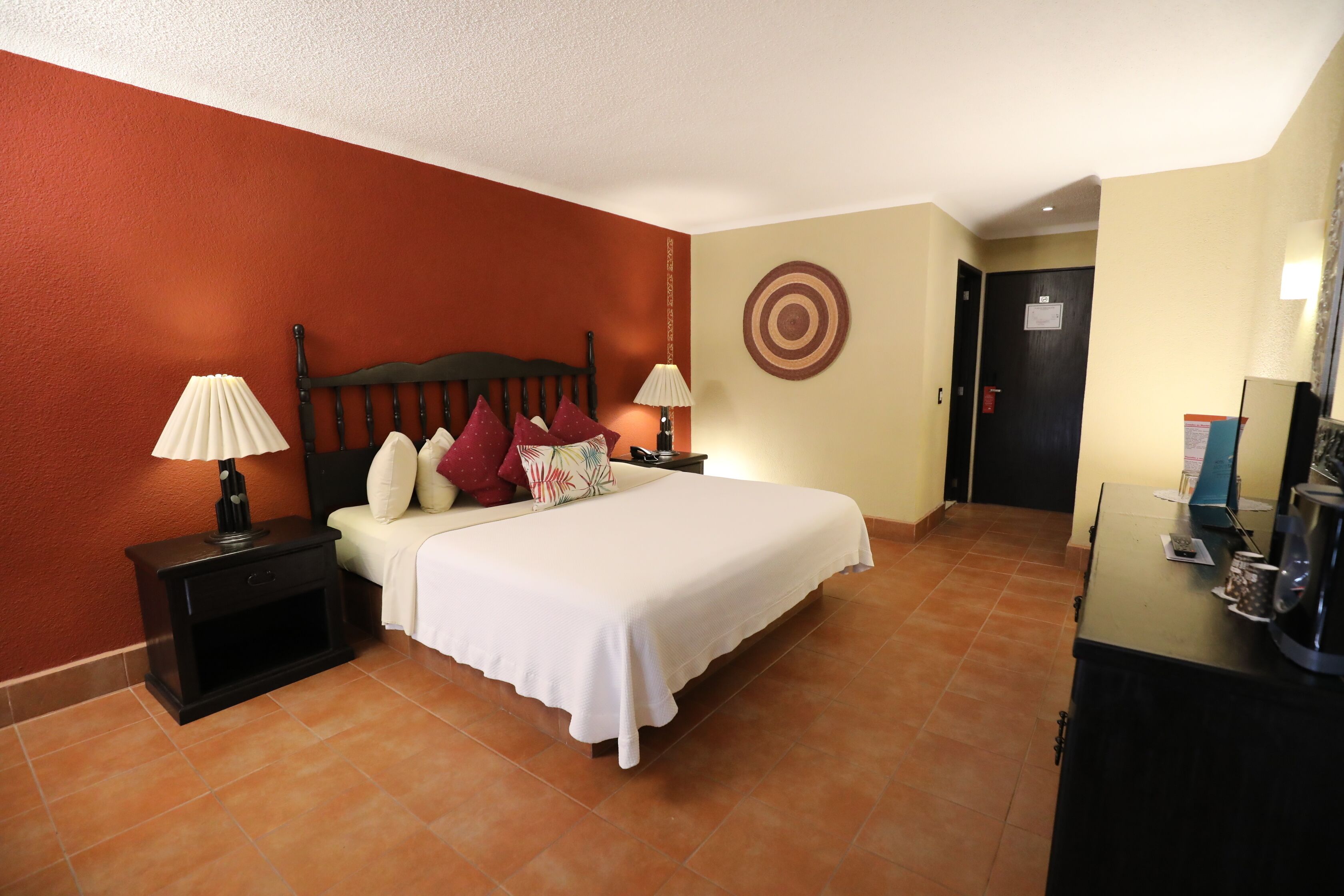 A hotel room with a bed, two bedside tables with lamps, a dresser, and a door.