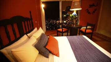 Habitación de hotel con cama, una silla, una mesa y vistas de la ciudad de noche.