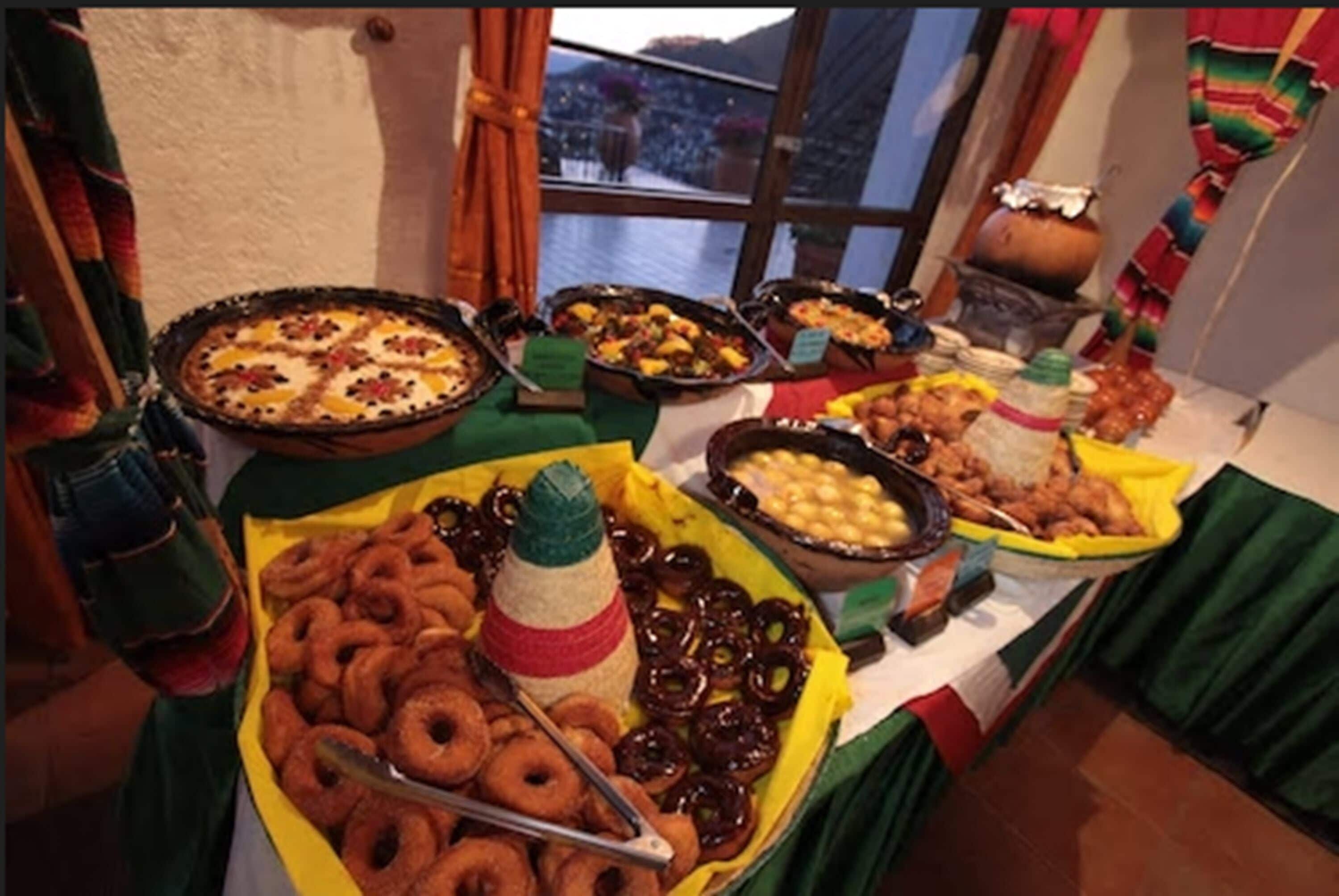Una mesa de buffet con distintos alimentos, incluyendo donas, pasteles y una olla grande.
