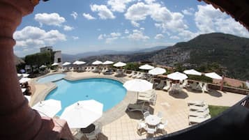 Un espace piscine doté de nombreuses chaises longues et de parasols, le tout entouré d’un paysage montagneux.