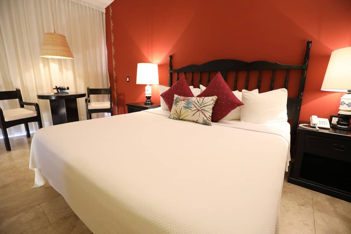 A hotel room with a large bed, two bedside tables with lamps, a chair, and a small table with a lamp.