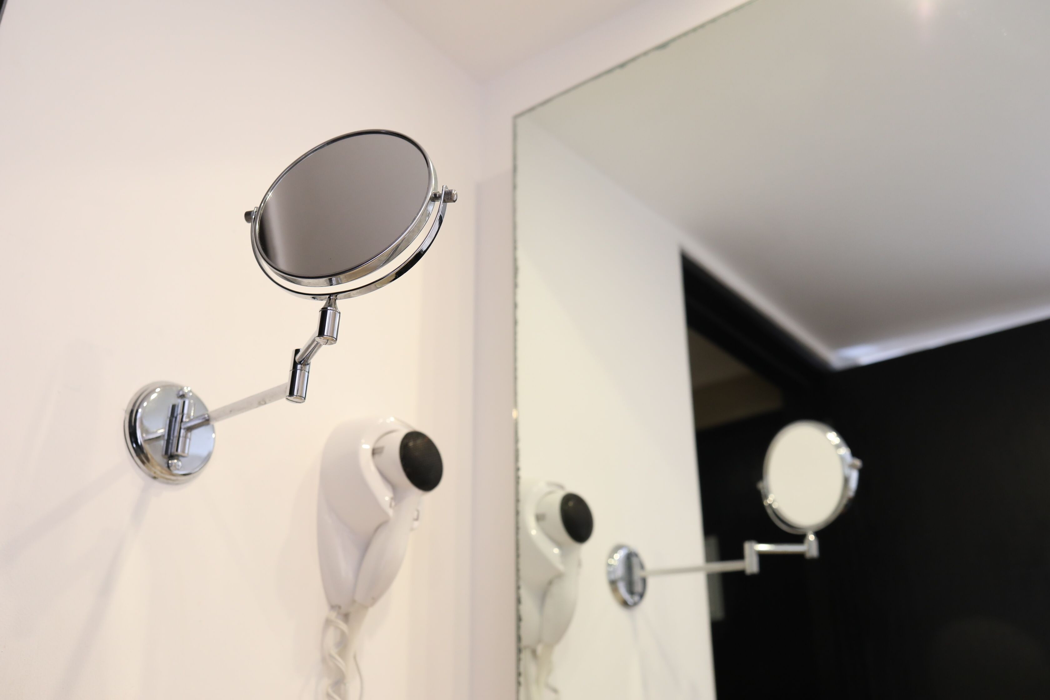A bathroom with a wall-mounted mirror, a hairdryer, and a towel rack.