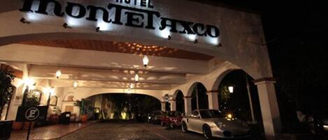 A hotel entrance with a sign reading "HOTEL MONTEAXCO" and a cobblestone driveway leading to parked cars.