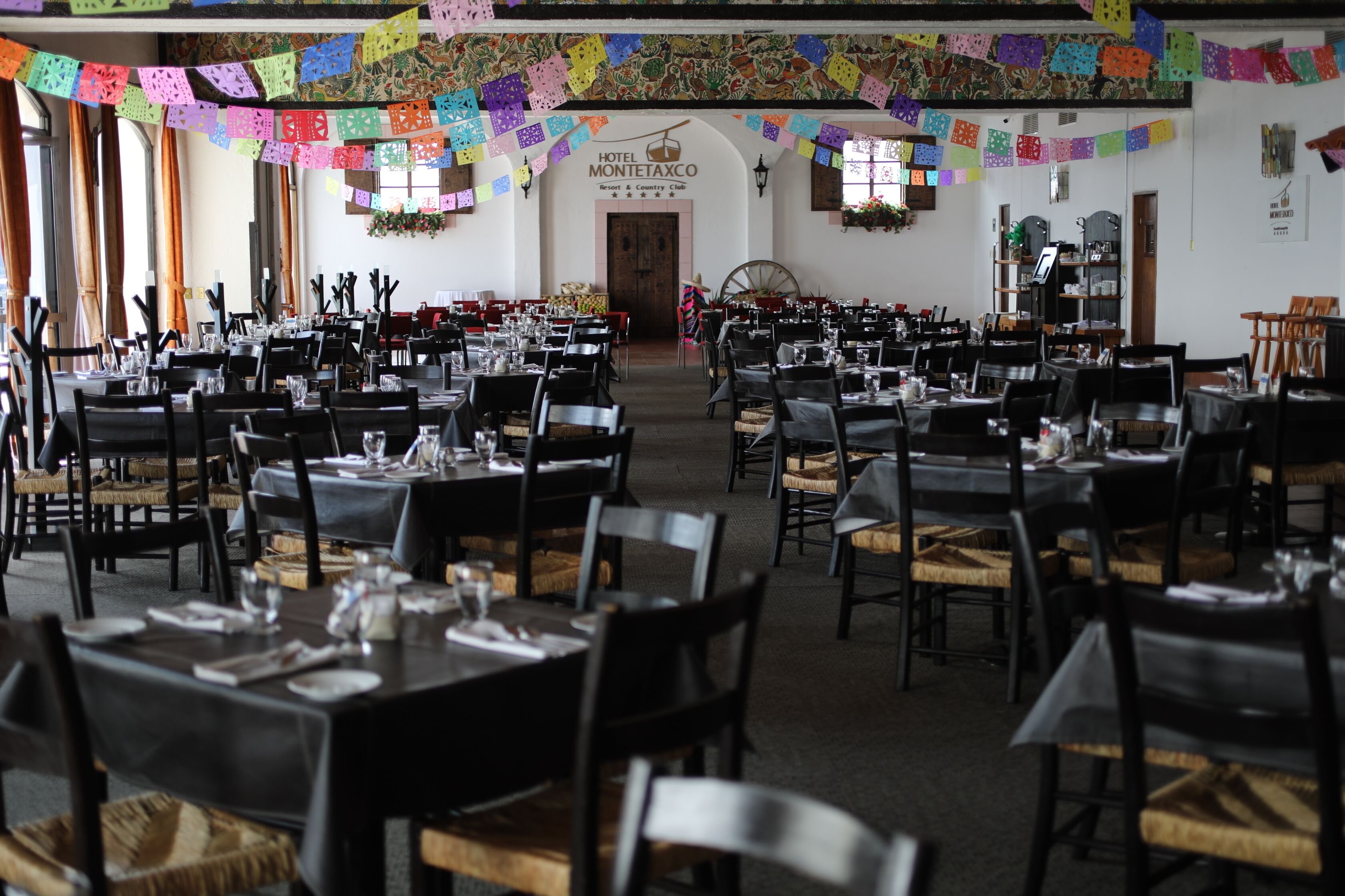 A large dining hall with multiple tables and chairs, decorated with colorful paper banners.