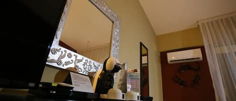 A hotel room with a large mirror, a coffee machine, a flat-screen TV, and an air conditioning unit.