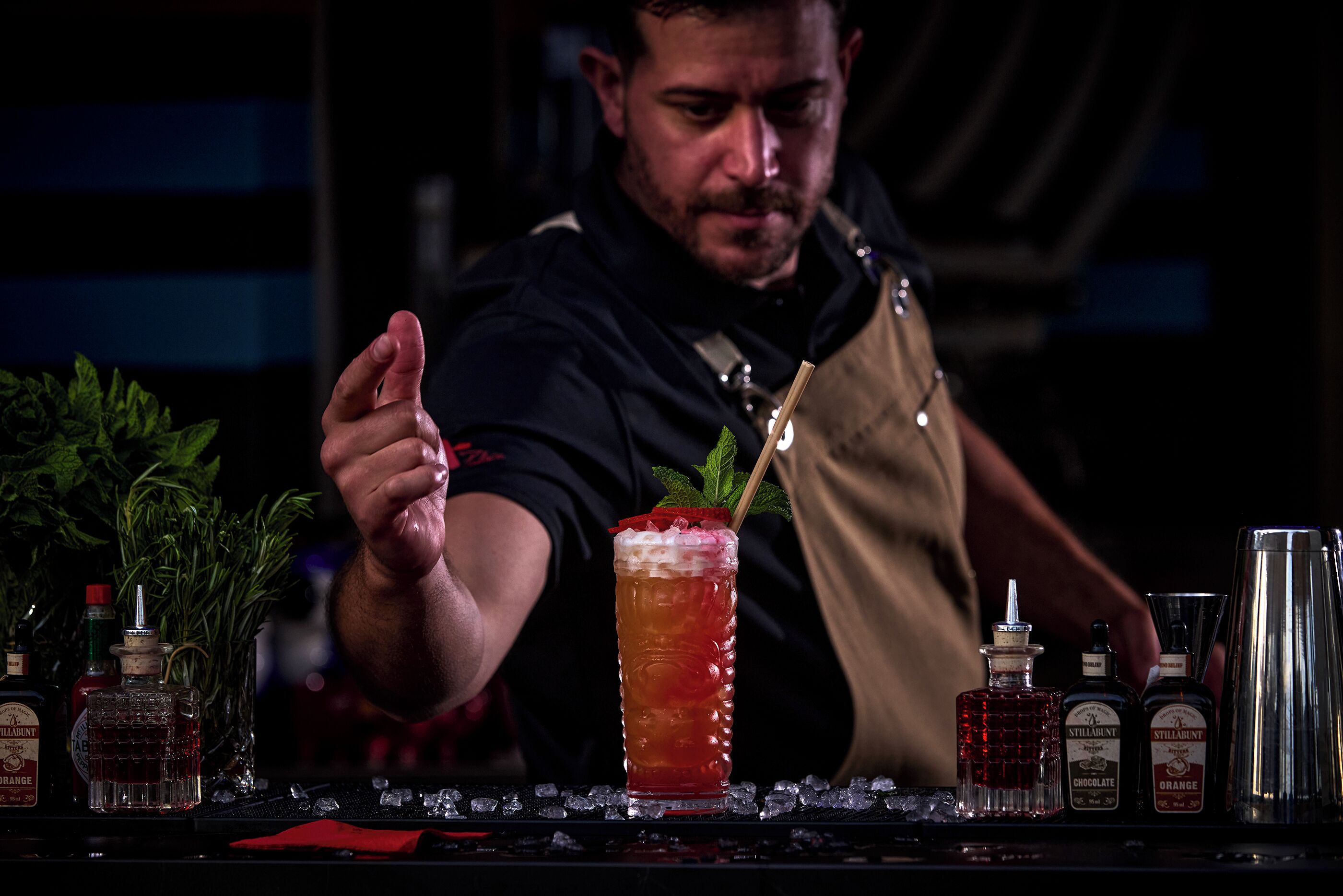 Ein Barkeeper bereitet einen Drink mit verschiedenen Flaschen und einem Glas auf der Bar zu.