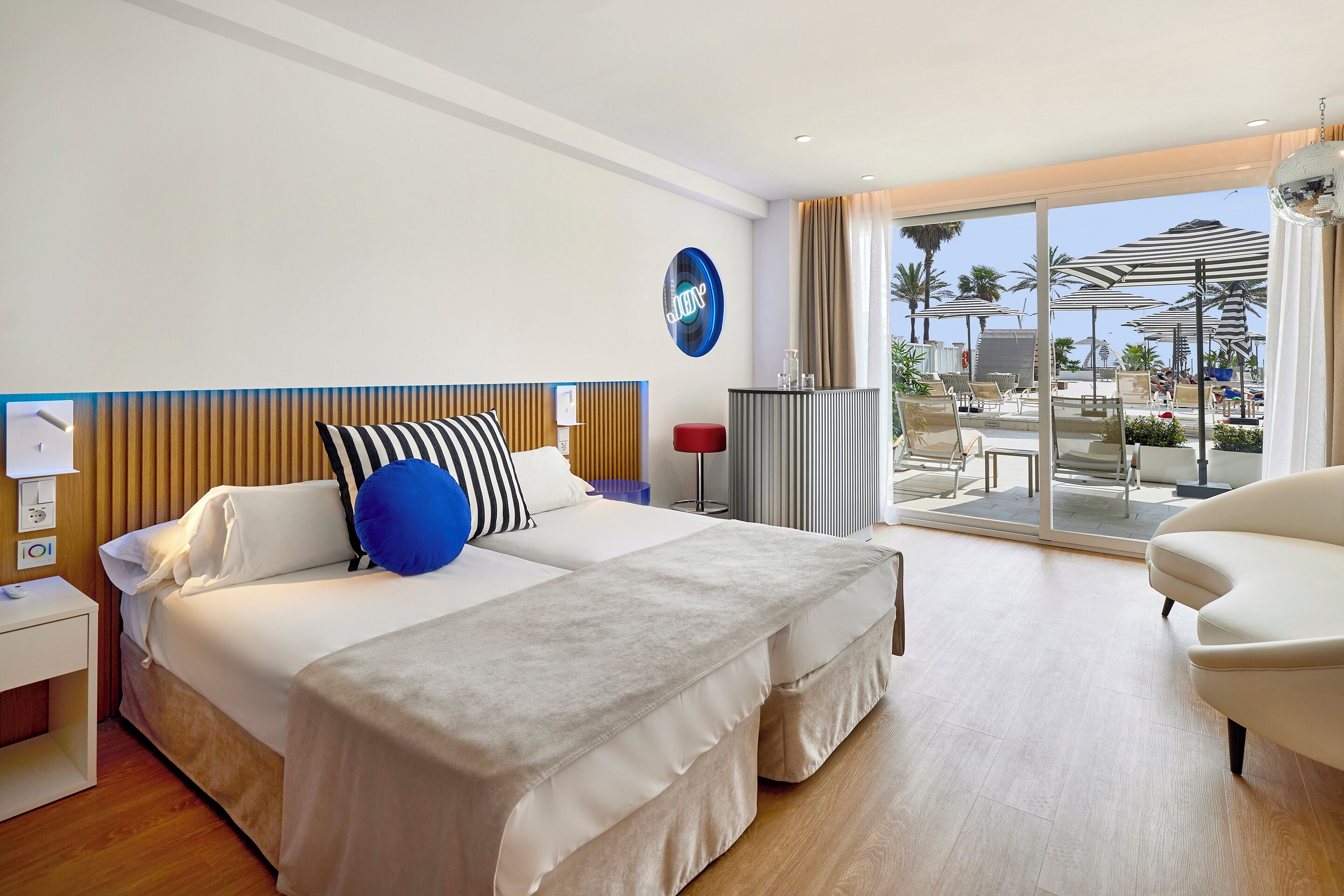 A modern hotel room with a large bed, a desk, and a view of the pool area.
