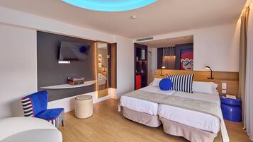 A modern hotel room with a large bed, a TV mounted on the wall, a seating area with a chair, and a small table.