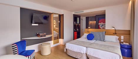Une chambre d’hôtel moderne dotée d’un grand lit, d’un téléviseur fixé au mur, d’un coin salon avec un fauteuil et d’une petite table.