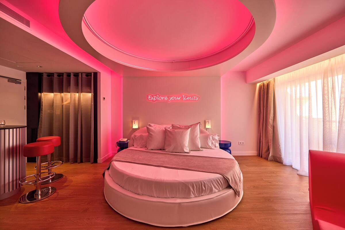 A modern bedroom with a circular bed, a bar area, and a neon sign.